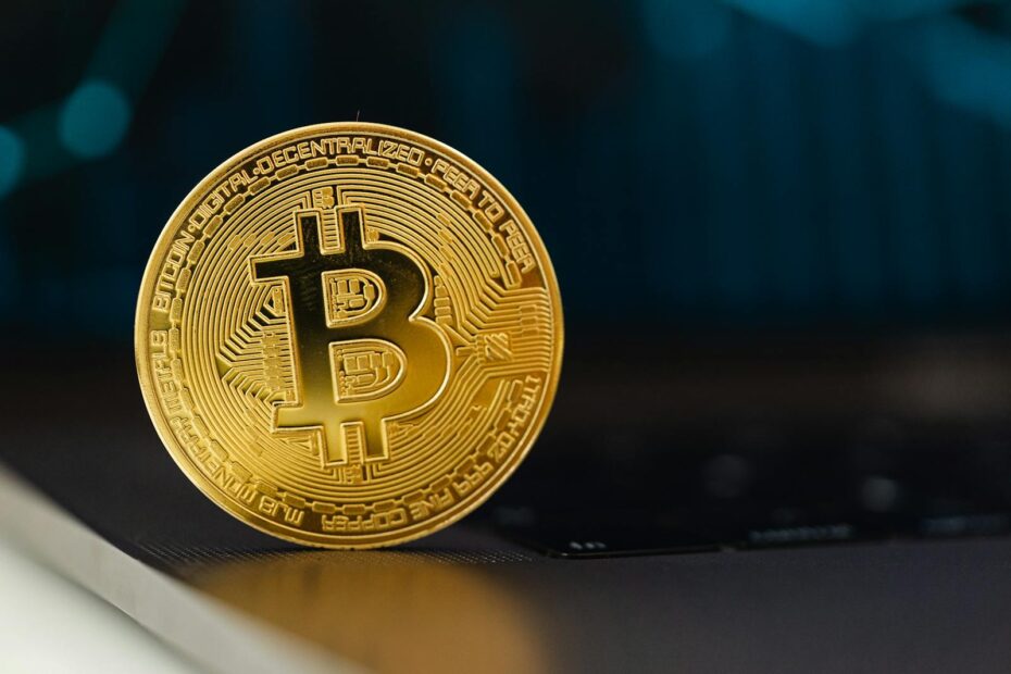 Golden Bitcoin coin standing upright on a laptop keyboard, representing digital currency.